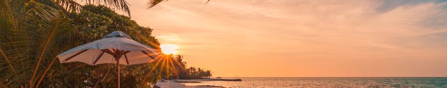 Sonnenliegen und -schirme an einem tropischen Strand bei Sonnenuntergang