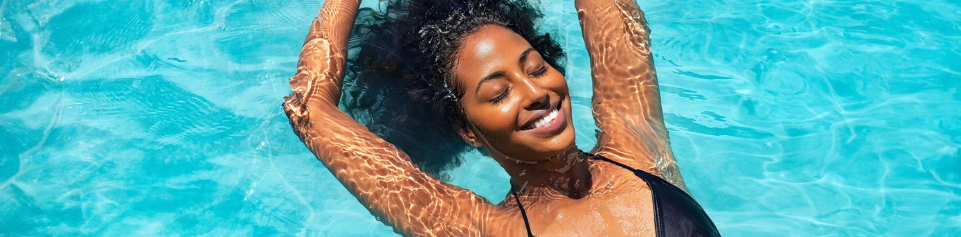 Eine Frau liegt lächelnd und mit geschlossenen Augen in einem Pool und entspannt sich