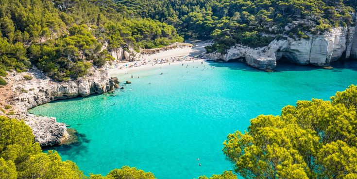 Küstenabschnitt und Strand mit Badegästen vor türkisblauem Wasser auf Menorca, Balearen, Spanien