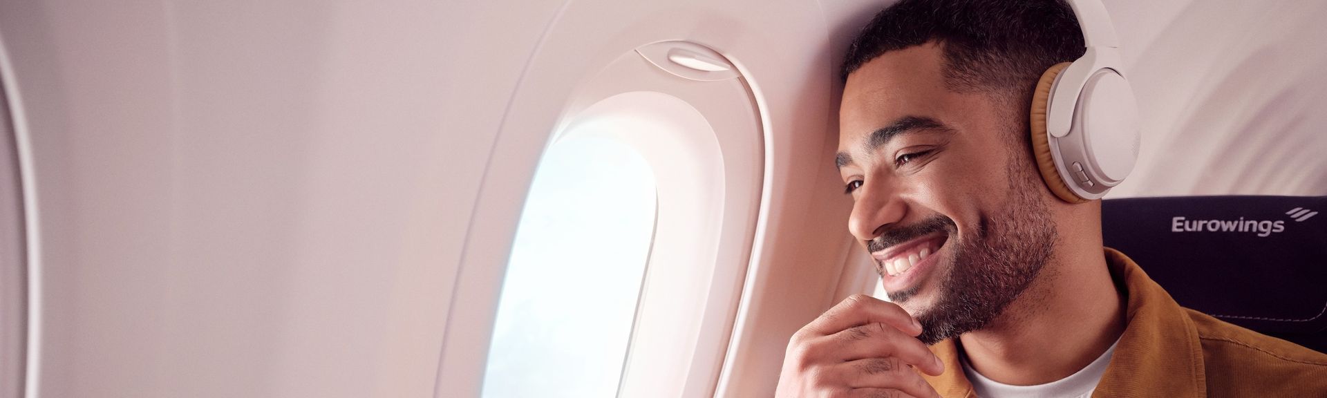 Mann mit Kopfhörern sitzt in einem Flugzeug und schaut lächelnd aus dem Fenster