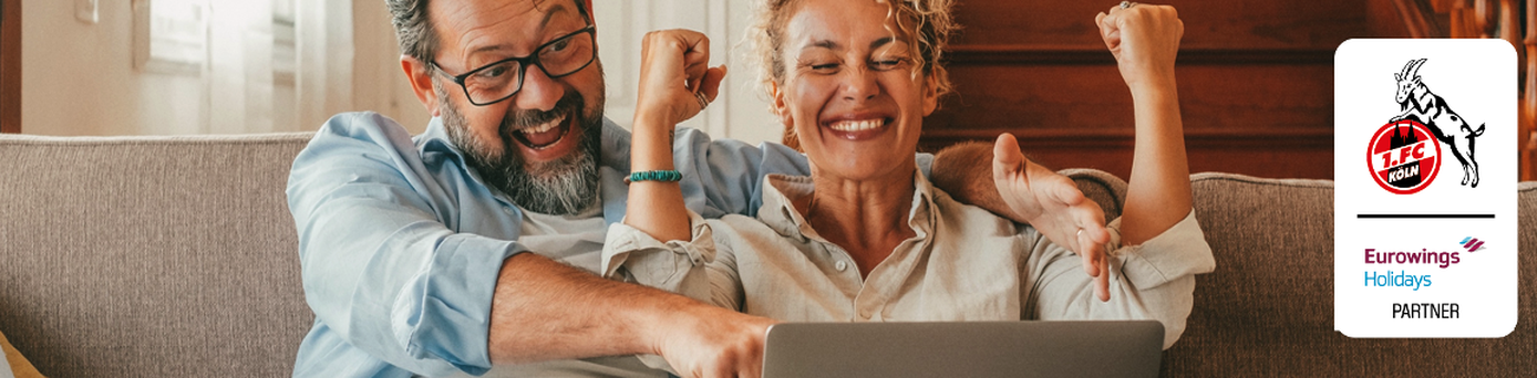 Ein Paar sitzt mit Laptop auf einem Sofa und freut sich