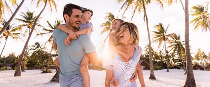 Familie mit zwei Kindern laeuft fröhlich an einem Strand entlang