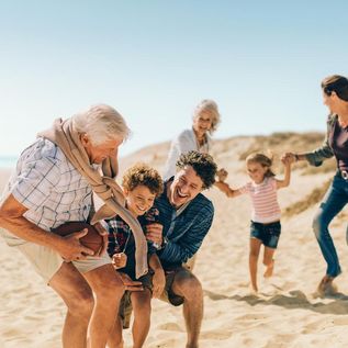 Familie mit Großeltern, Eltern und Kindern tollt ausgelassen an einem Strand herum