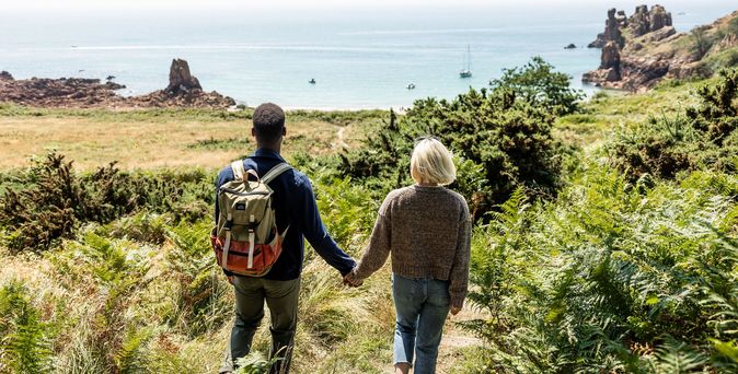 Ein Paar steht an der grün bewachsenen Küste Jerseys und blickt aufs Meer.