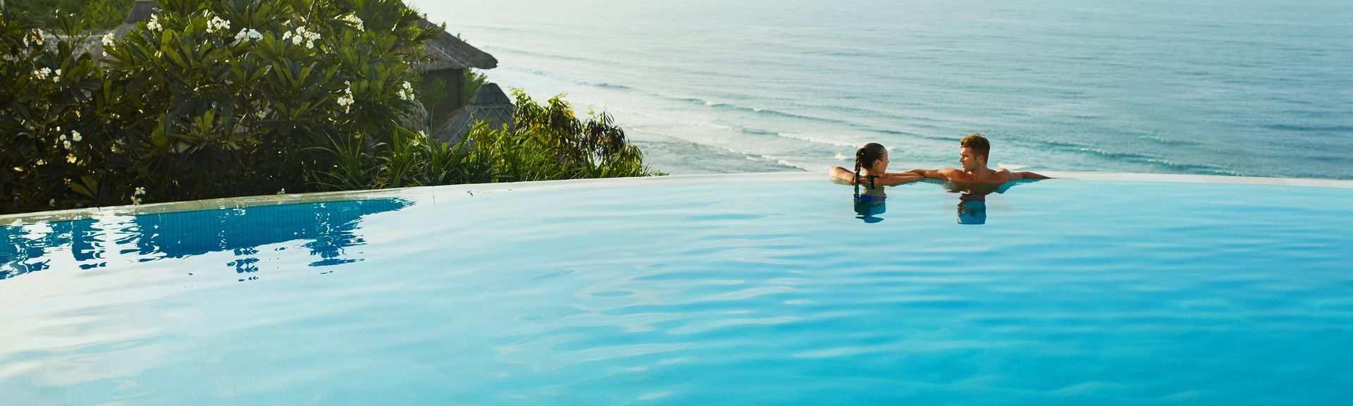Ein Paar relaxt in einem Infinity Pool direkt am Strand