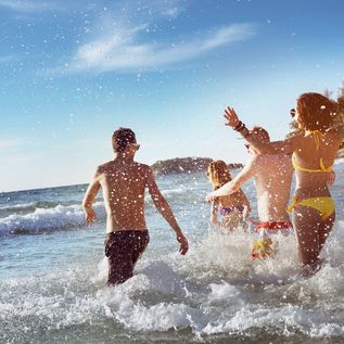 Eine Freundesgruppe rennt fröhlich ins Meer bei strahlendem Sonnenschein