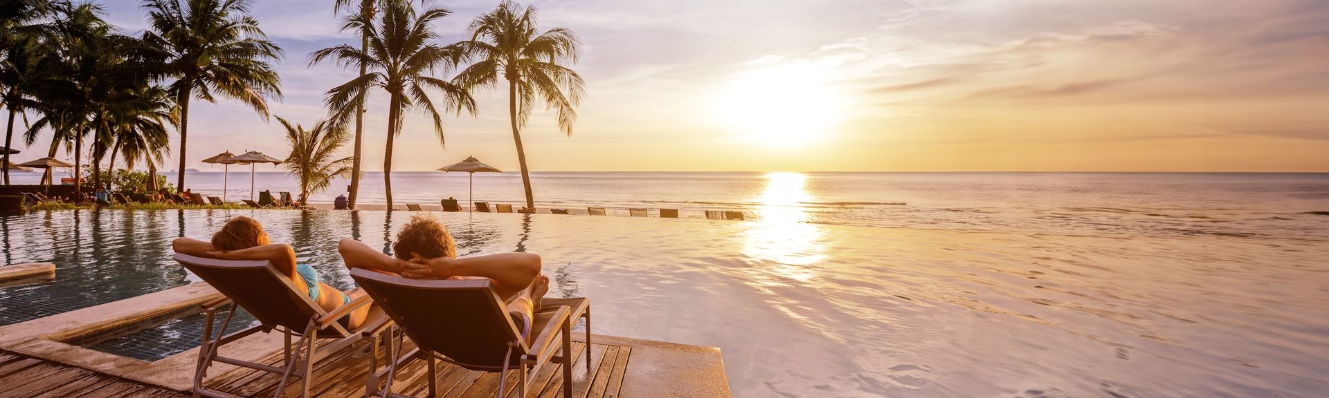 Ein Paar liegt an einem tropischen Pool und blickt auf den Sonnenuntergang über dem Meer