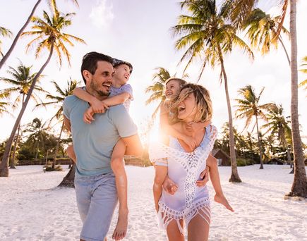 Familie mit zwei Kindern laeuft fröhlich an einem Strand entlang