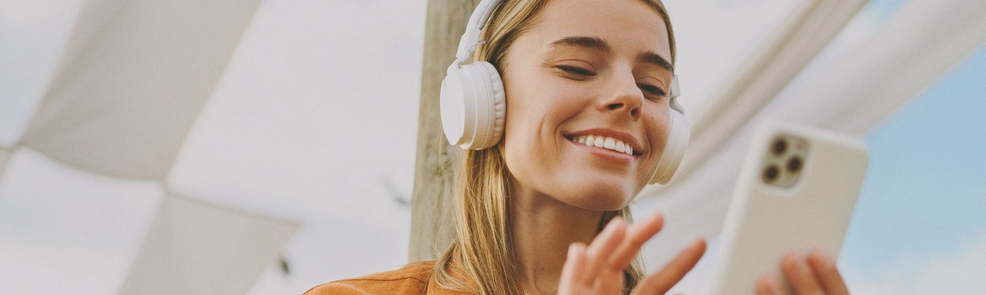 Junge Frau mit Kopfhörern schaut lächelnd auf ihr Smartphone