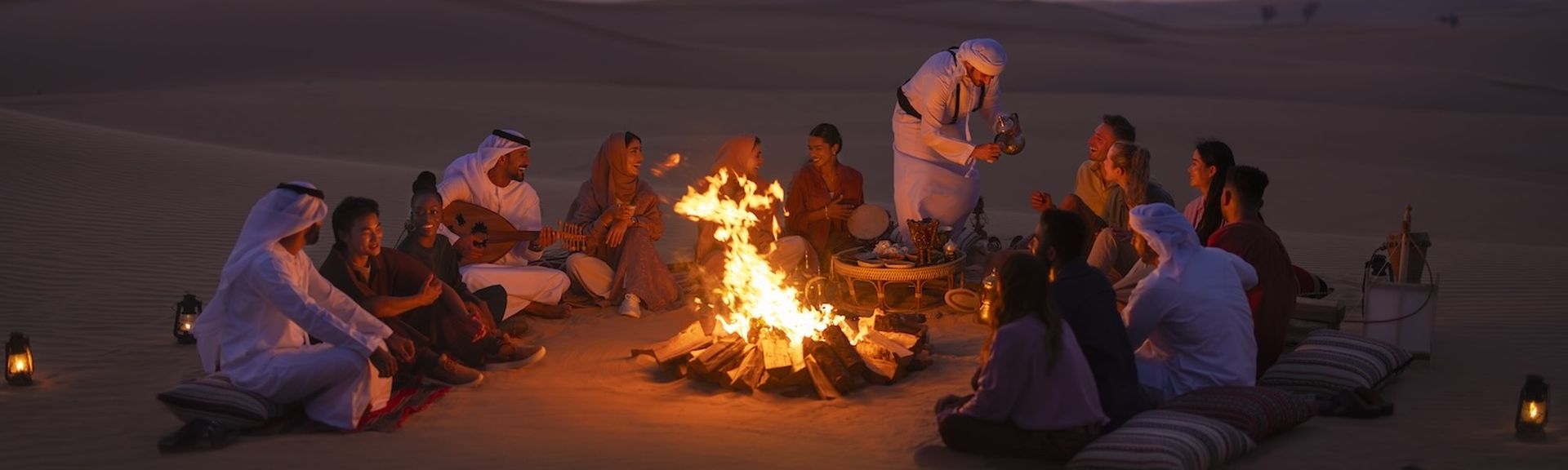 Eine Gruppe von Guides und Gästen sitzen um ein Lagerfeuer in der Wüste Abu Dhabis