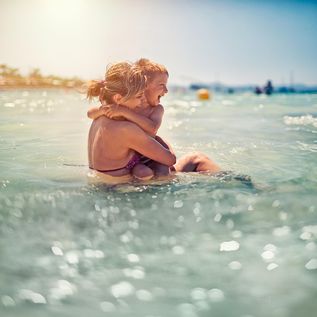 Mutter und Kind sitzen am Strand in den Wellen