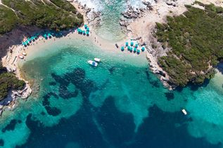 Vogelperspektive auf eine türkisblaue Bucht mit Booten und Schirmen in Albanien