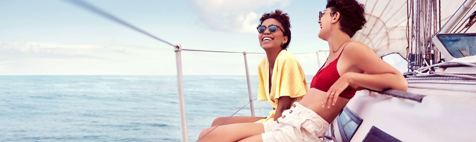 Zwei junge Frauen sitzen am Rande einer Yacht und lachen ausgelassen